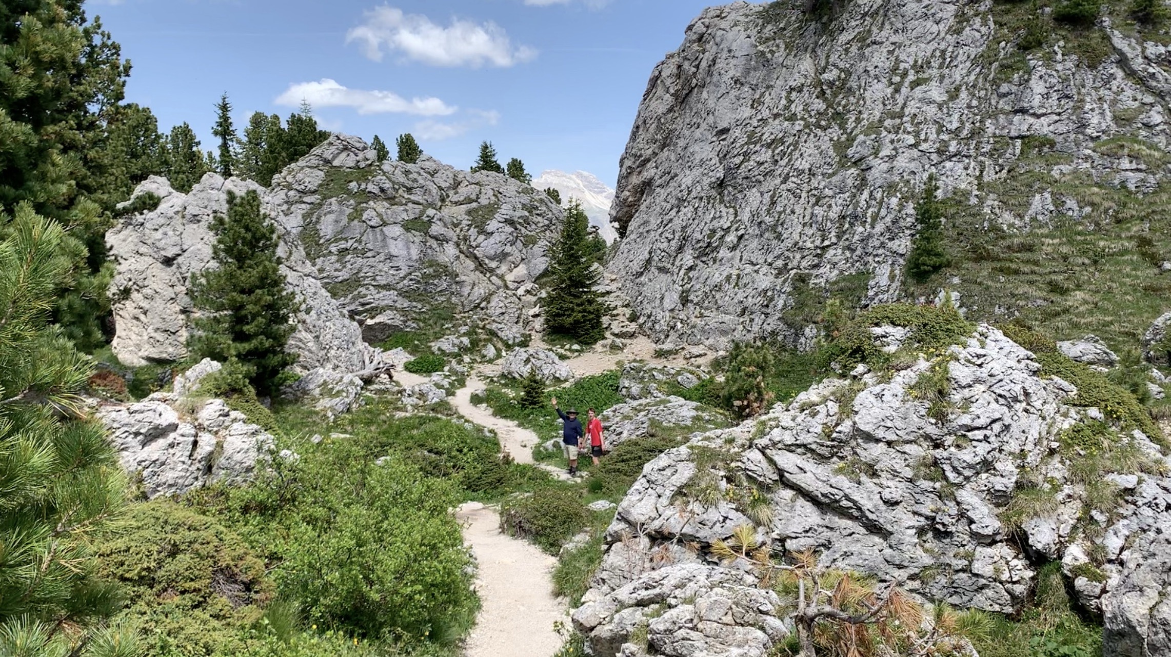 two hikers walk on a trail in between large rocks