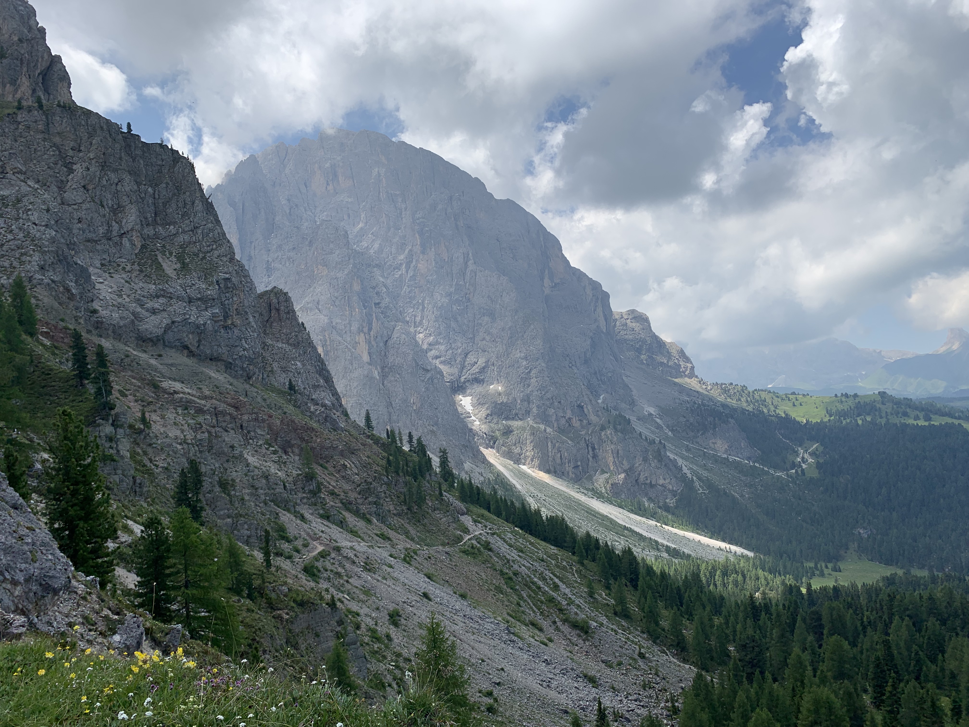 two hikers walk along a trail that hugs the side of a scree-full mountain