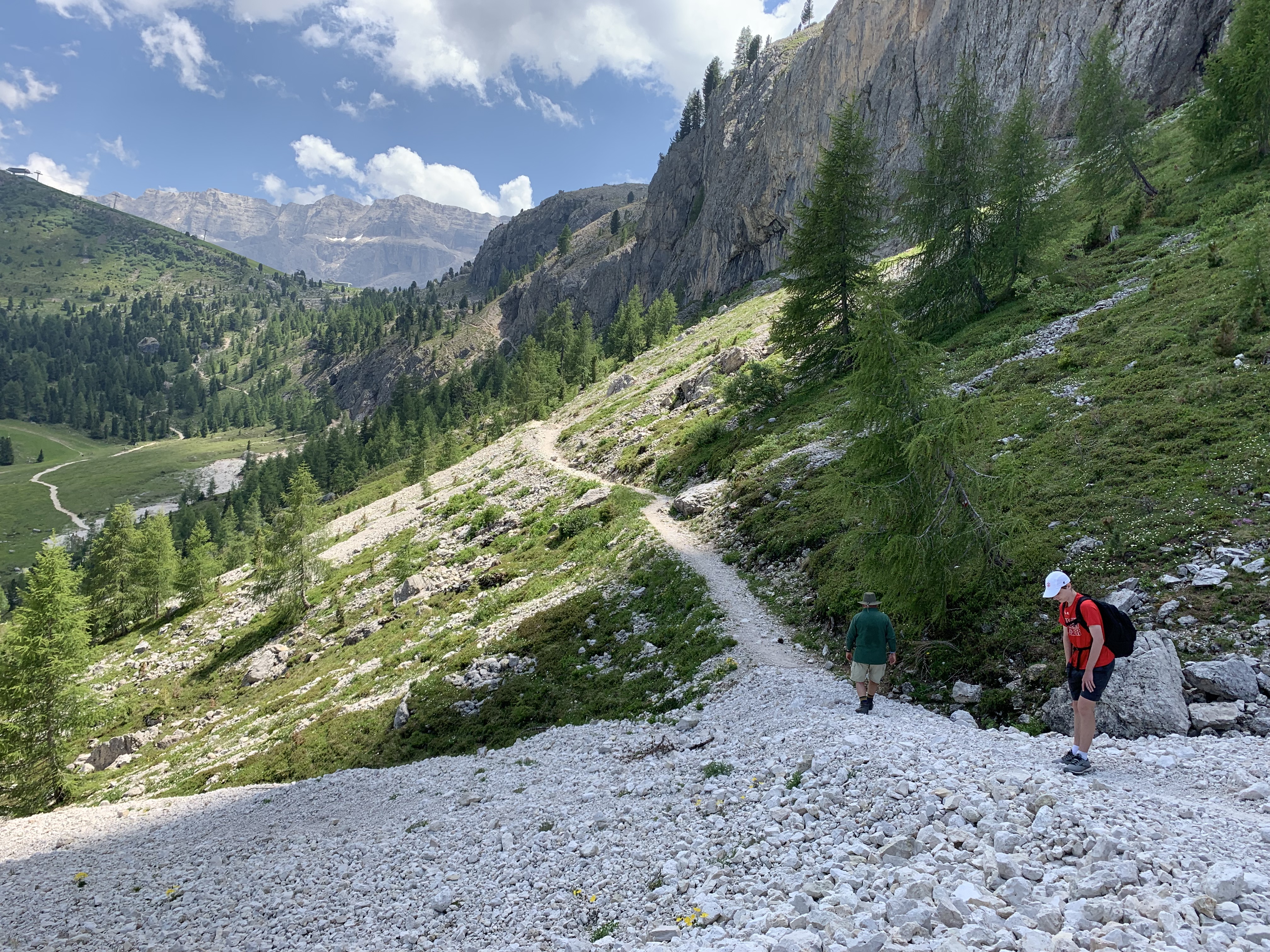 two hikers walk along a trail that hugs the side of a scree-full mountain