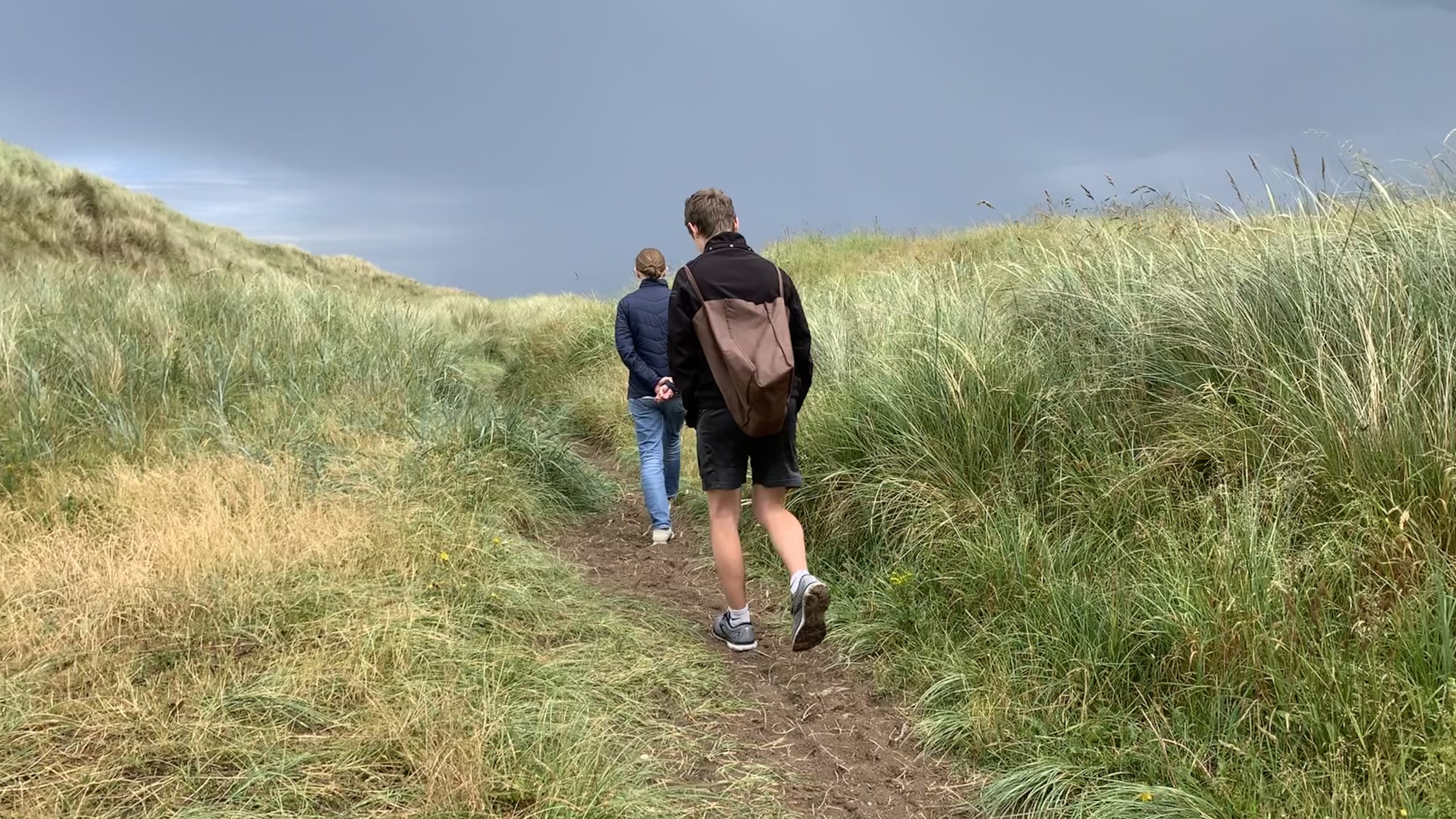 a man and woman walk on a path through grassy dunes